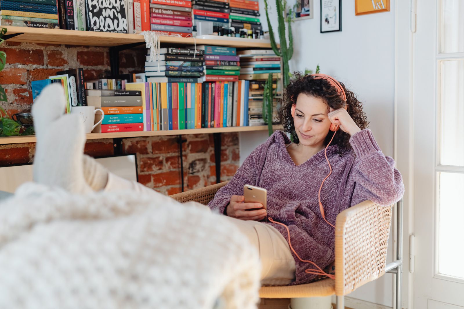 Afbeelding van een vrouw zittend op een stoel met koptelefoon op en smartphone in de hand